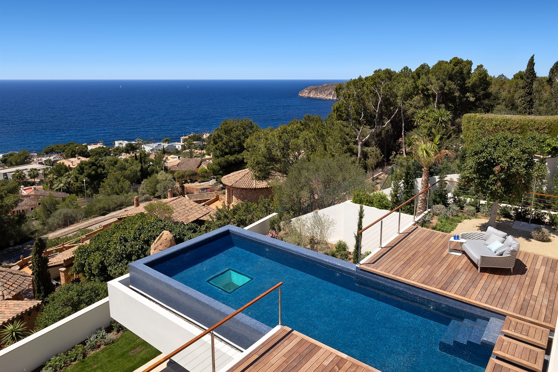 Ein Blick aus dem Obergeschoss der Luxusvilla nahe Port d’Andratx auf die weitläufige Terrasse, den meerblauen Infinitypool und die Bucht von Palma.