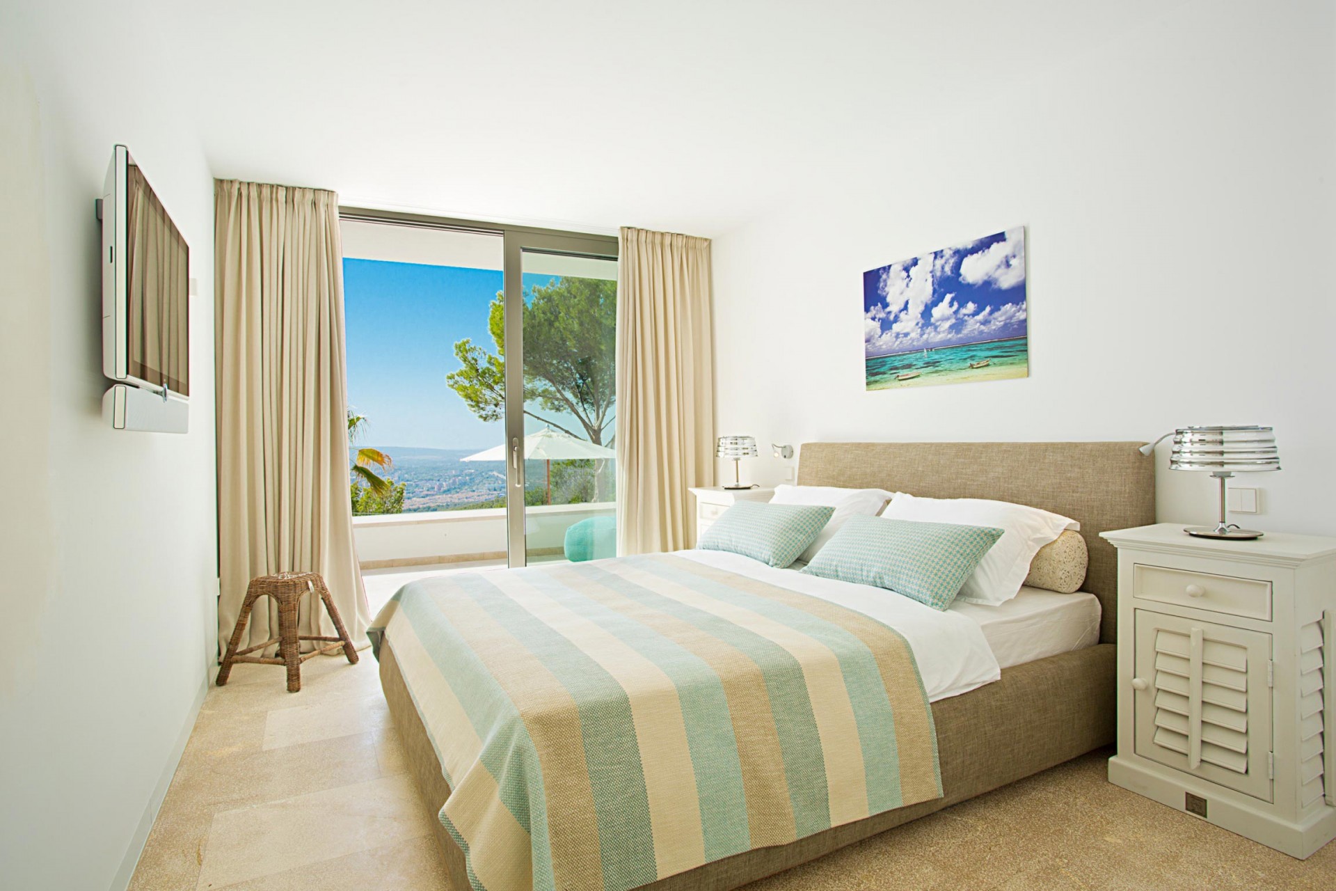 Das hell gehaltene Gästezimmer mit dezenten pinken Akzenten. Durch die geöffnete Glastür erkennt man den Panorama-Blick auf die Südwest-Küste Mallorcas bei Puerto Portals.